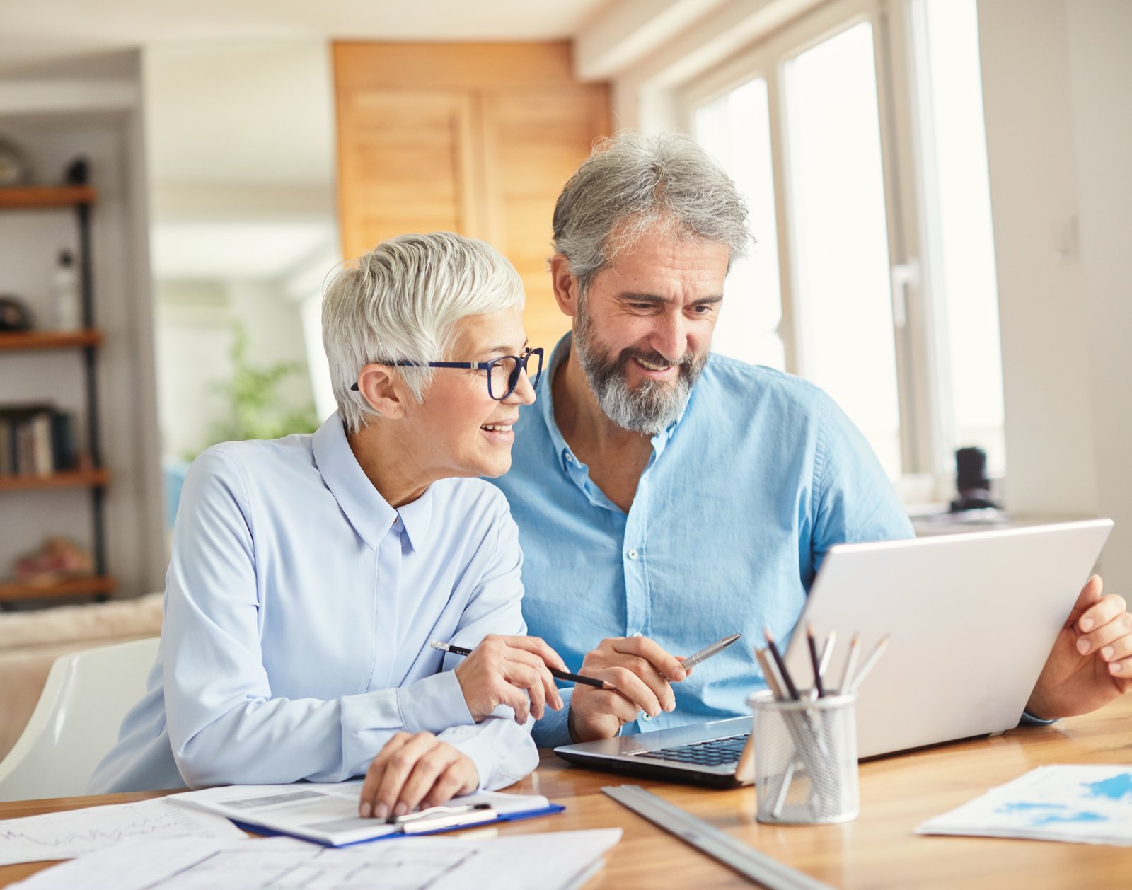 Older couple discussing finances and life insurance options while reviewing documents and using a laptop at home.