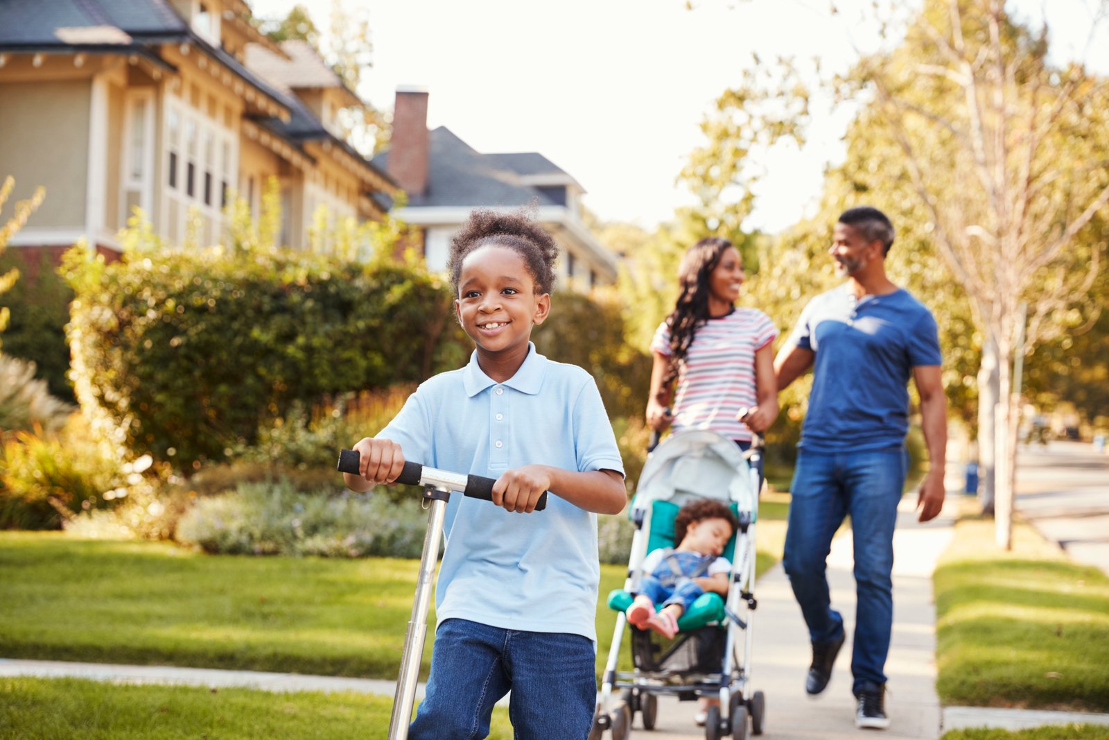 Family enjoying a walk in a suburban neighborhood, with a child riding a scooter and parents pushing a stroller, reflecting community and family life in Lakewood Ranch.